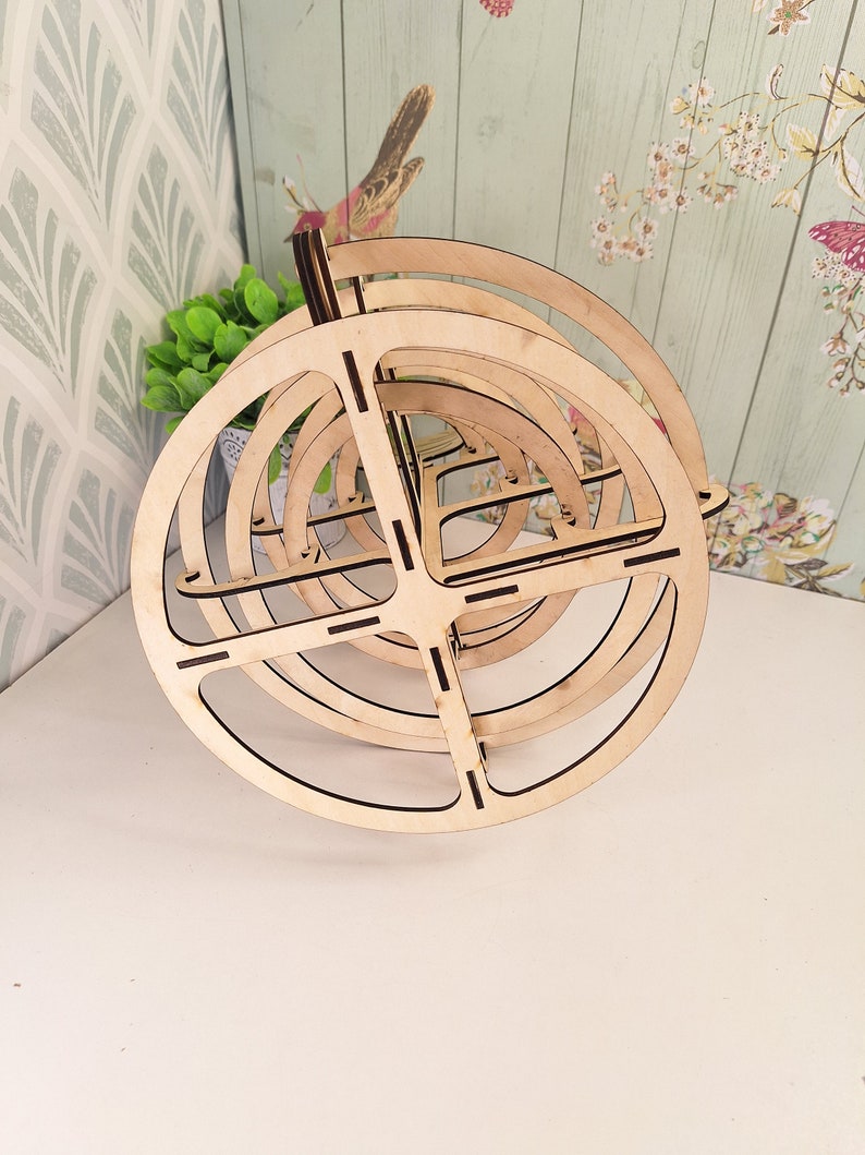 May include: A wooden, circular, multi-tiered stand with a natural wood finish. The stand is made of several concentric circles that are stacked on top of each other.