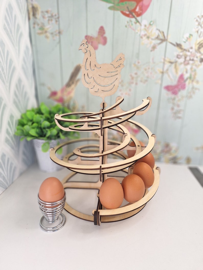 May include: Wooden egg holder shaped like a spiral with a chicken on top. The holder is made of natural wood and has a rustic look. It can hold up to 6 eggs.