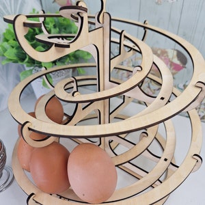 May include: A wooden egg holder shaped like a spiral with a bird on top. The holder is made of light wood and has a natural finish. There are three brown eggs in the holder.