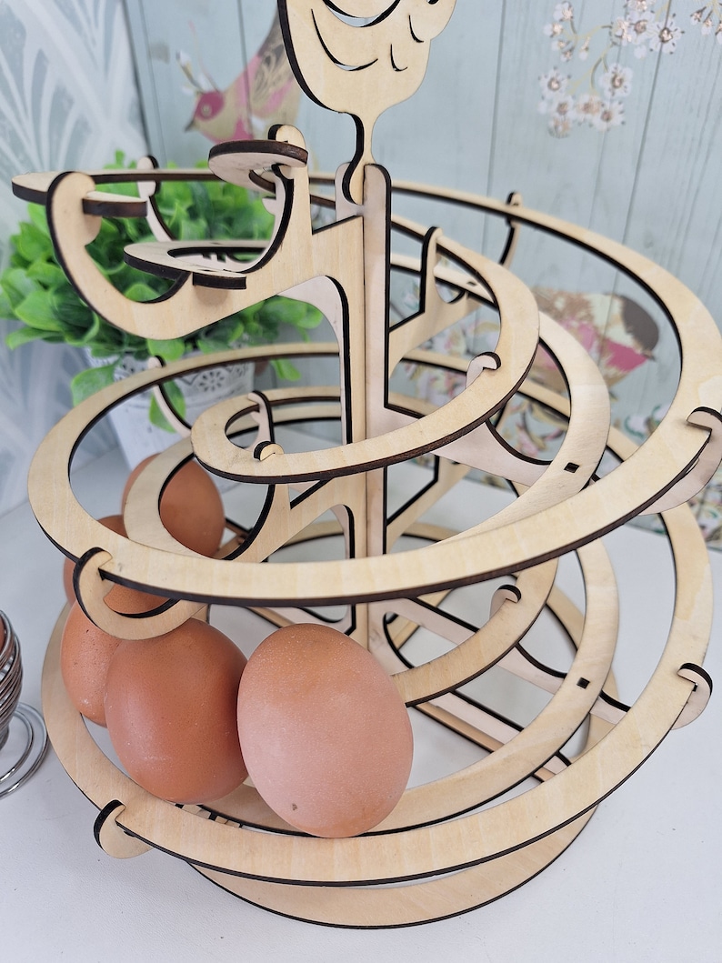 May include: A wooden egg holder shaped like a spiral with a bird on top. The holder is made of light wood and has a natural finish. There are three brown eggs in the holder.