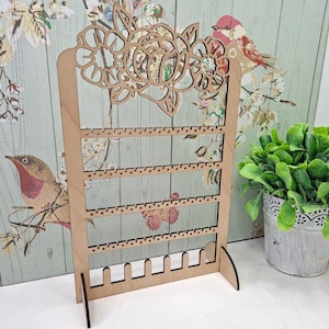 May include: A wooden earring display stand featuring a floral design at the top. The stand has multiple rows of small holes for hanging earrings. The natural wood colour complements the decorative floral cutout, creating an elegant and functional jewellery organiser.
