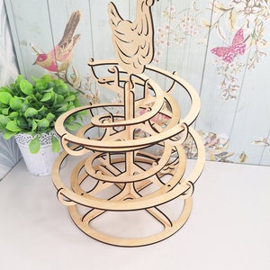May include: Wooden egg holder shaped like a spiral with a chicken on top. The holder is made of light brown wood and has a circular base.