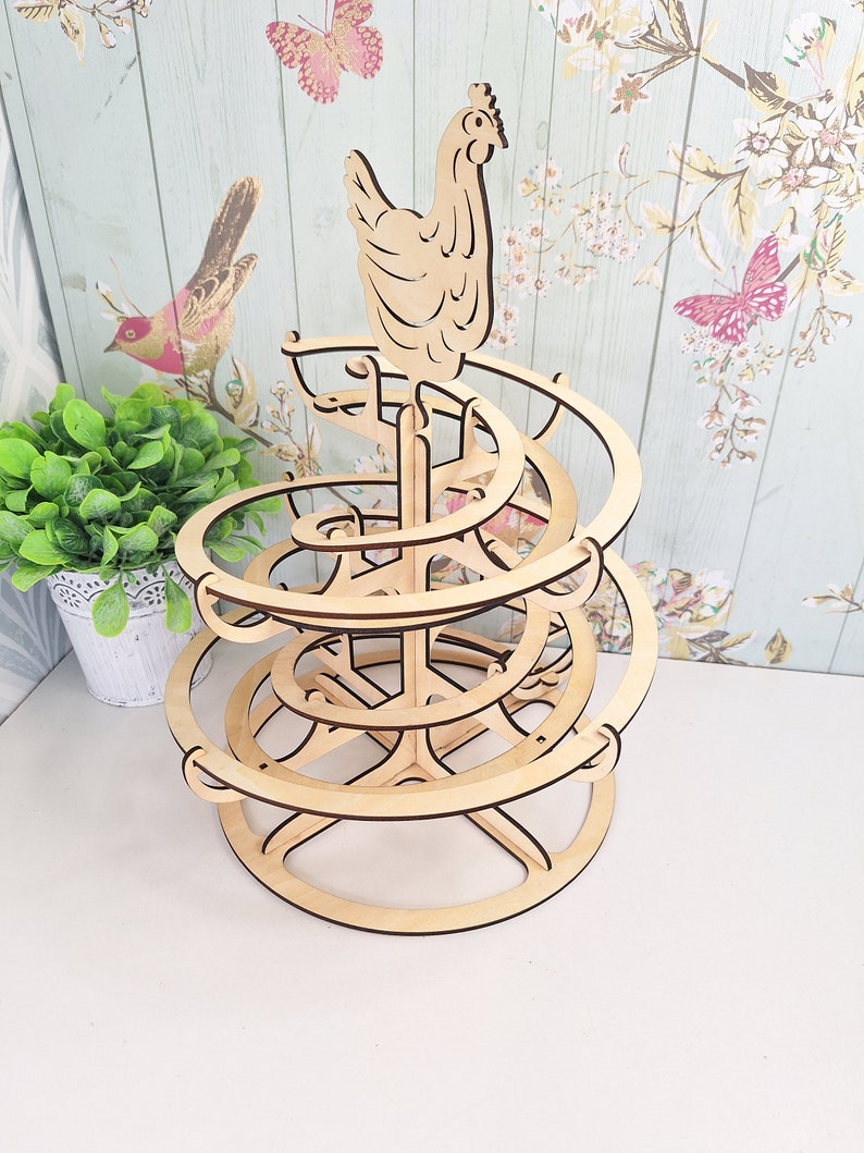 May include: Wooden egg holder shaped like a spiral with a chicken on top. The holder is made of light brown wood and has a circular base.