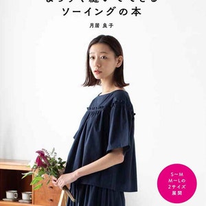 May include: A book cover with a woman wearing a dark blue top and skirt, holding a bouquet of flowers. The title of the book is "まっすぐ縫いでできる ソーイングの本" and the author is "月居 良子". The book cover also includes the text "S~M M~Lの 2サイズ 展開" and "日本ヴォーグ社 Heart Warming Life Series".