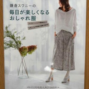 May include: A book cover with a white background and a woman wearing a white shirt and a patterned skirt. The book title is "鎌倉スワニーの 毎日が楽しくなる おしゃれ服" which translates to "Kamakura Swan's Everyday Fun Fashion".