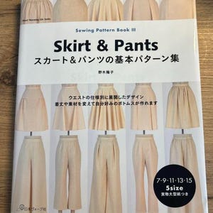 Op de afbeelding: Een boek getiteld "Skirt & Pants" met de Japanse tekst "スカート&パンツの基本パターン集" en "野木陽子". De omslag van het boek toont illustraties van verschillende rokken en broeken in een licht beige kleur. De tekst "7-9-11-13-15 5size 実物大型紙つき" is ook zichtbaar op de omslag.
