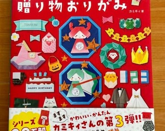 May include: A red book with the title "カミキィの気持ちが伝わる 贈り物おりがみ" (Kamiki's feelings are conveyed origami gifts) and a picture of various origami creations. The book is the third in a series and has sold over 200,000 copies.