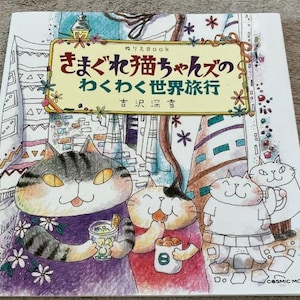 May include: A colourful book cover with the title "きまぐれ猫ちゃんズのわくわく世界旅行" (Kimagure Neko-chanzu no Wakuwaku Sekai Ryokou) which translates to "Whimsical Cat's Exciting World Trip". The cover features illustrations of cats in various settings, including a cityscape and a cafe.