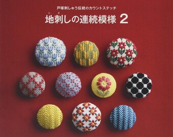 Puede incluir: Una portada de libro con el título "Jishi no Zenshu Keisho 2" en japonés. La portada presenta un fondo rojo con 10 botones redondos bordados de colores.