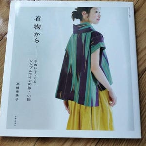 May include: A book cover with a woman wearing a green and purple patterned shirt and a yellow skirt. The book title is "着物から" which translates to "From Kimono" in English. The text below the title reads "手ぬいでつくる シンプルラインの服・小物" which translates to "Hand-sewn simple line clothes and accessories". The author's name is "高橋恵美子" which translates to "Emiko Takahashi".