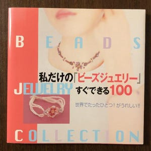 Może przedstawiać: Różowa i niebieska książka zatytułowana "BEADS" z tekstem "Moje "koralikowe ozdoby" 100 łatwych projektów" i "Kolekcja" na okładce. Książka zawiera zdjęcie kobiety noszącej naszyjnik z koralików i bransoletkę z koralików.