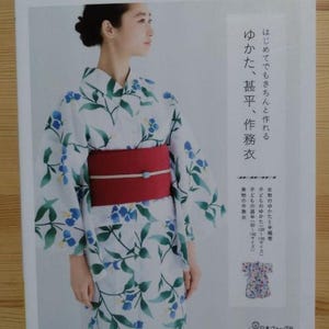 May include: A white yukata with a floral pattern of blue flowers and green leaves. The yukata is worn by a person with a red obi sash. The text on the page reads "はじめてでもきちんと作れる ゆかた、甚平、作務衣" which translates to "Even beginners can make it. Yukata, Jinbei, and Samue."