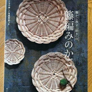 Peut inclure: Un livre intitulé "籐編みのかご" avec le texte "籐かご教室『紡ぎ』の" sur la couverture. Le livre présente trois paniers tissés, deux ronds et un ovale, avec une feuille verte sur l'un des paniers.