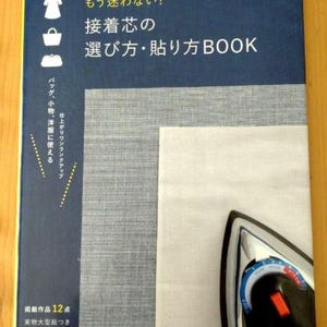 以下が含まれることがあります： 「もう迷わない！接着芯の選び方・貼り方BOOK」というタイトルの青い本と、白い布の上に置かれたアイロンの画像です。