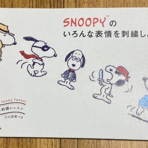 May include: A white book with a black and white illustration of Snoopy on the cover. The book is titled "Snoopy's Different Expressions Embroidery Lesson".