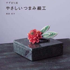 Könnte beinhalten: Ein Buchcover mit einer grünen Marmorbox und einer roten Blume darauf. Der Titel des Buches lautet "やさしいつまみ細工", was mit "Einfache Blumenhandwerke" übersetzt werden kann. Der Name des Autors ist "栗原宏予", was "Hiroyo Kurihara" bedeutet.