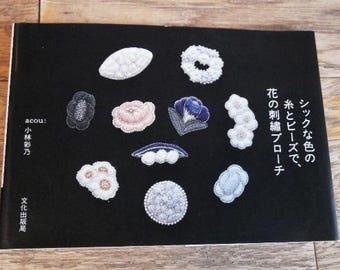 Puede incluir: Una colección de broches bordados con varios diseños florales y geométricos. Los broches están hechos con cuentas e hilo en tonos de blanco, negro, rosa, azul y verde. El texto en la página dice "シックな色の糸とビーズで、花の刺繍ブローチ".