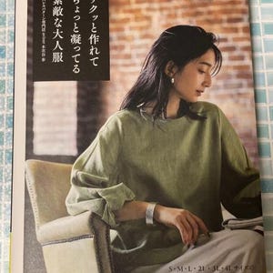 Pode incluir: Uma capa de revista com uma mulher vestindo uma blusa verde de manga comprida. O texto na capa diz "Heart Warming Life Series" e texto japonês. A revista também inclui informações de tamanho: S, M, L, 2L, 3L e 4L.