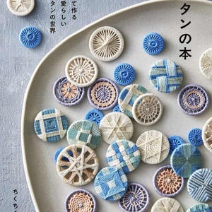 Peut inclure: Assortiment de boutons faits à la main, aux motifs variés et aux couleurs bleu, blanc et beige. Les boutons sont disposés sur une assiette grise, avec du texte japonais. Les boutons sont fabriqués avec du fil et présentent des motifs complexes.
