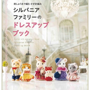 Puede incluir: Un libro con una portada rosa y el título "Sylvanian Families Dress-up Book" en japonés. El libro presenta patrones de crochet para hacer ropa para las figuras de Sylvanian Families. La portada muestra cinco atuendos de crochet para las figuras, incluyendo un oso marrón, un gato, un conejo, un ratón y un gato.