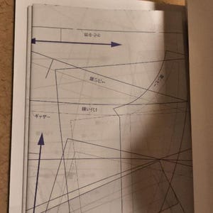Pu&ograve; includere: Un cartamodello di cucito in bianco e nero con testo giapponese, tra cui "キサツ" (che significa "forbici") e "袖付け1" (che significa "attacco manica 1").