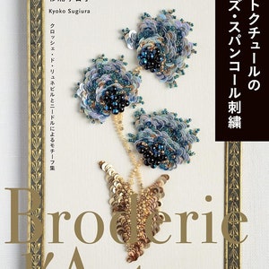 Può includere: Una copertina di libro con una cornice dorata e il titolo "Broderie d'Art" in grandi lettere stilizzate. La copertina presenta un primo piano di un ricamo di perline con tre fiori in tonalità blu e oro.