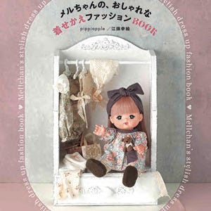 Peut inclure: Une couverture de livre représentant une poupée aux cheveux bruns portant une robe à fleurs. Le titre du livre est "Mellchan's Stylish Dress Up Fashion Book" et le sous-titre est "Vêtements pour poupée de 26 cm". La couverture du livre est rose et blanche avec un motif en forme de cœur.