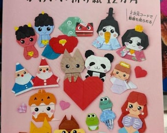 May include: A book cover with a pink background and colorful origami figures. The title is "Cute Origami 12 Months" in Japanese. The book features a variety of origami figures, including a panda, a fox, a mermaid, and a frog.