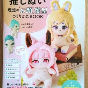 Puede incluir: Un libro en japonés con un juguete de peluche rosa, blanco y marrón en la portada. El título del libro es "推しぬい 理想のお顔 髪型 つくりかたBOOK", que se traduce como "Libro de cómo hacer un peinado y un rostro ideal para un peluche".