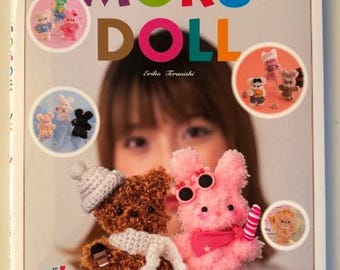 Puede incluir: Portada del libro "MORU DOLL" con letras coloridas. La imagen muestra varias muñecas hechas a mano, incluido un oso de peluche marrón con bufanda y gorro, y un conejito rosa con gafas de sol.