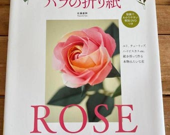 May include: A book cover featuring a paper rose. The cover has the word "ROSE" in large pink letters. The book's title is in Japanese, with a photo of a pink and orange paper rose. The book is about origami.