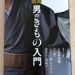 Pode incluir: Capa de livro com texto japonês e foto de pessoa usando um quimono. A capa é predominantemente preta. O título é "Introdução ao quimono masculino". O livro também apresenta informações sobre materiais e amarrações.