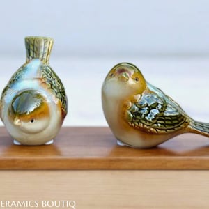 May include: Two ceramic bird figurines. One is a round bird with green, blue, and brown glaze. The other is a brown and green bird with a long tail.