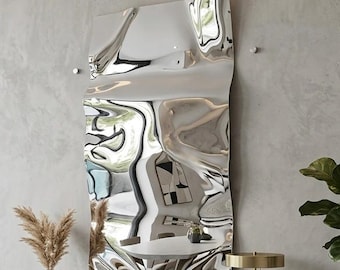 May include: A rectangular wall mirror with a highly reflective, distorted, and wavy surface. The mirror is mounted on a light gray wall above a dark wood sideboard. The reflective surface creates a liquid-like appearance, warping the room's interior.