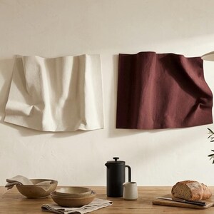 Puede incluir: Escena de comedor con una mesa de madera con cuencos, pan y una cafetera. Dos paneles de tela, uno crema y otro burdeos, están montados en la pared. Un jarrón con vegetación y una lámpara colgante completan la decoración.