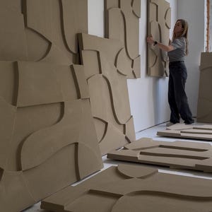 Puede incluir: Piezas de arte mural abstractas beige con formas geométricas. Algunas piezas están montadas en una pared blanca, otras están en el suelo. El arte tiene una estética moderna y minimalista. Las piezas están hechas de un material sólido.
