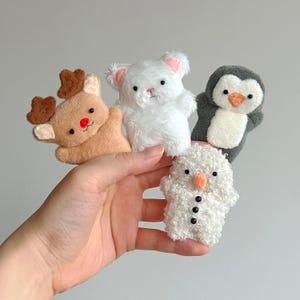 May include: A collection of small, plush Christmas ornaments. The ornaments include a reindeer with brown antlers and a red nose, a white bear, a penguin, and a snowman with a carrot nose and black buttons.
