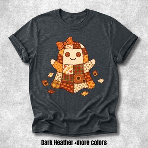 Könnte beinhalten: Ein dunkelgrau meliertes Kurzarm-T-Shirt mit einer zentralen Grafik eines Geistes, der aus Patchwork-Stoffquadraten in herbstlichen Orange-, Braun- und Gelbtönen besteht. Der Geist hat Knopfaugen, ein gesticktes Lächeln und eine orangefarbene Schleife.