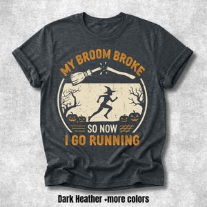 May include: A dark heather gray short-sleeve t-shirt featuring a graphic print with the text MY BROOM BROKE SO NOW I GO RUNNING. The design includes a broken broomstick, a silhouette of a running witch, bare trees, and pumpkins in orange.