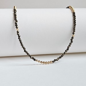 May include: A delicate gold and black beaded necklace with a row of gold beads in the center.