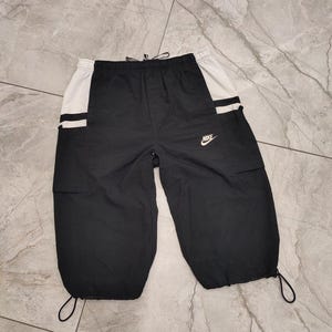 May include: Black cargo pants with white side panels and a Nike logo. The pants have a drawstring waist and a cuffed hem.