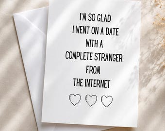 Könnte beinhalten: Eine weiße Grußkarte mit passendem Umschlag. Auf der Karte steht "I'M SO GLAD I WENT ON A DATE WITH A COMPLETE STRANGER FROM THE INTERNET" und drei Herzsymbole. Die Karte liegt auf einem neutralen Hintergrund.