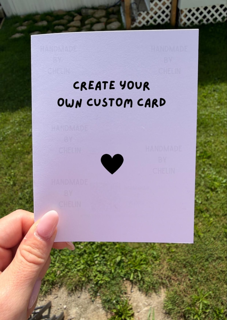 May include: A white rectangular card featuring the black text "CREATE YOUR OWN CUSTOM CARD" centered at the top, with a solid black heart icon positioned below the text. The background of the card contains a faint repeating watermark text.