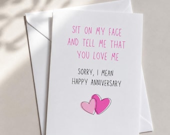 May include: A white greeting card with the text "SIT ON MY FACE AND TELL ME THAT YOU LOVE ME. SORRY, I MEAN HAPPY ANNIVERSARY" in pink and black. Two pink hearts are at the bottom. The card is inside a white envelope.
