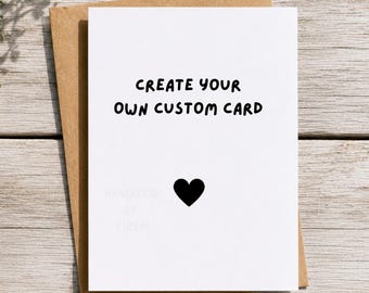 May include: A white greeting card with the black text CREATE YOUR OWN CUSTOM CARD and a small black heart icon centered below. The card is placed on top of a brown kraft paper envelope. The text Handmade By Chelin appears at the bottom.
