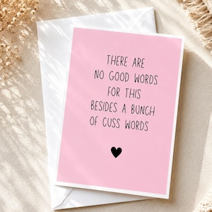 May include: A pink greeting card with the text "THERE ARE NO GOOD WORDS FOR THIS BESIDES A BUNCH OF CUSS WORDS" and a black heart. The card is inside a white envelope.