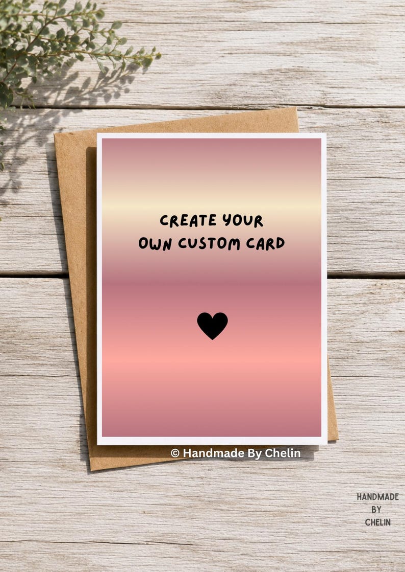 May include: A rectangular greeting card with a pink and peach gradient background. The text "CREATE YOUR OWN CUSTOM CARD" is printed in black, centered above a small black heart icon. The card is placed on top of a brown paper envelope.