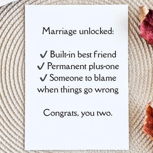 May include: A white card with the text "Marriage unlocked: Built-in best friend, Permanent plus-one, Someone to blame when things go wrong. Congrats, you two." on a textured background.