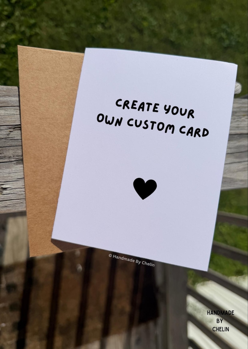 May include: A white greeting card with the black text CREATE YOUR OWN CUSTOM CARD and a small black heart icon below it. The card is paired with a light brown kraft paper envelope. The text Handmade By Chelin appears at the bottom of the card.