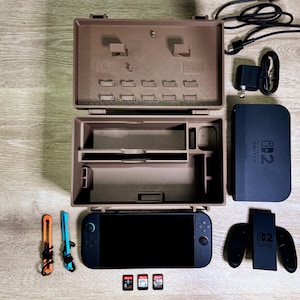 May include: A brown Nintendo Switch case, open to show internal compartments. A black Nintendo Switch console, controllers, game cartridges, and charging accessories are arranged around the case. The case is approximately 30 cm long.